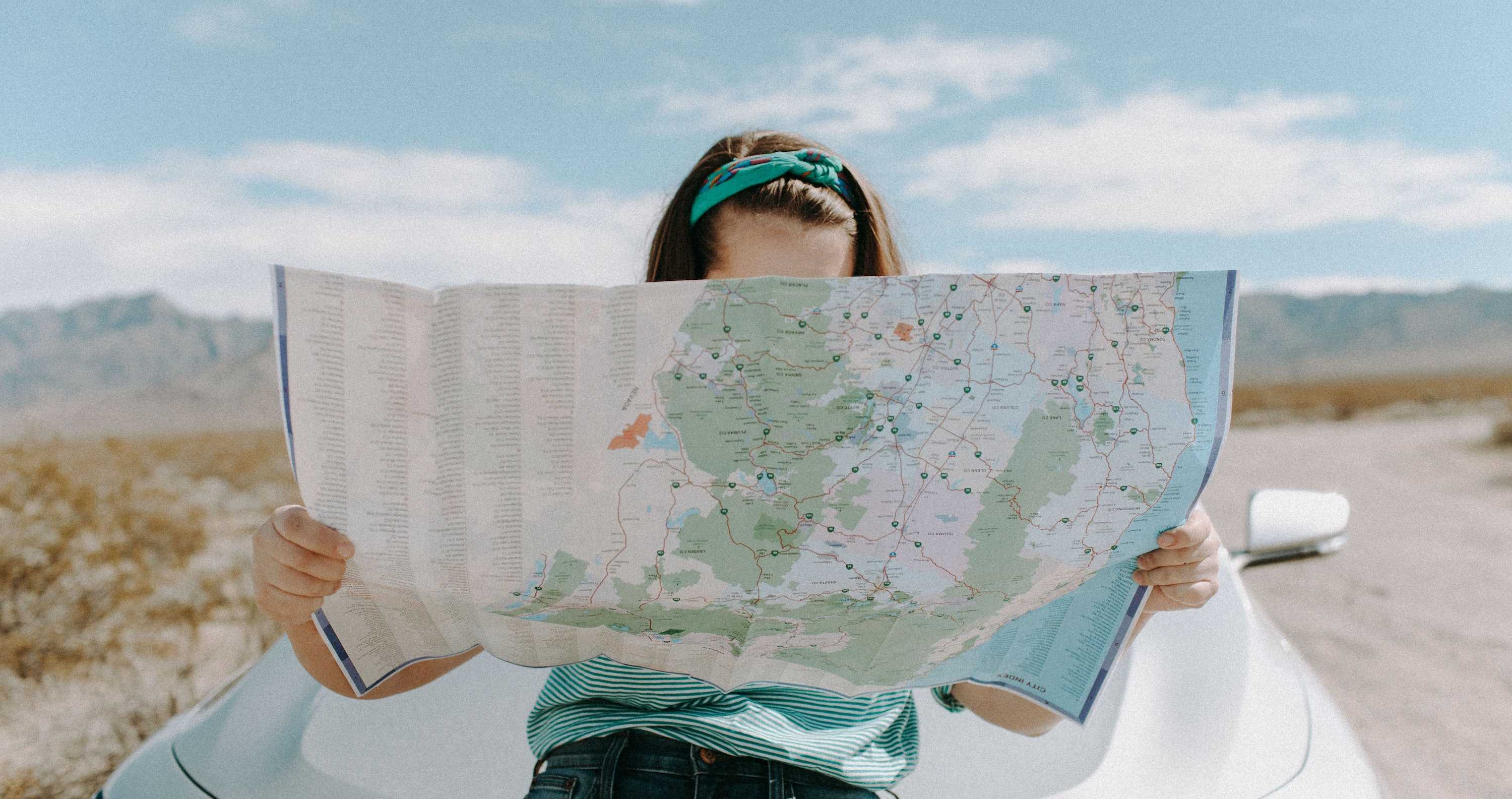 a woman leaning on a car holding a map in front of her face.