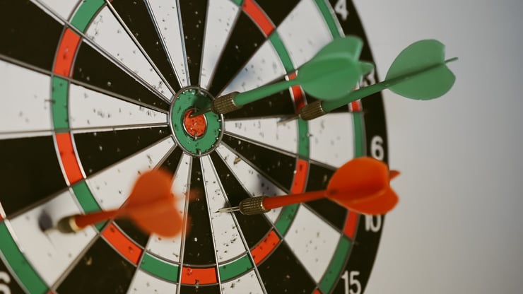 photo of a dart board with two red and two green darts in it.