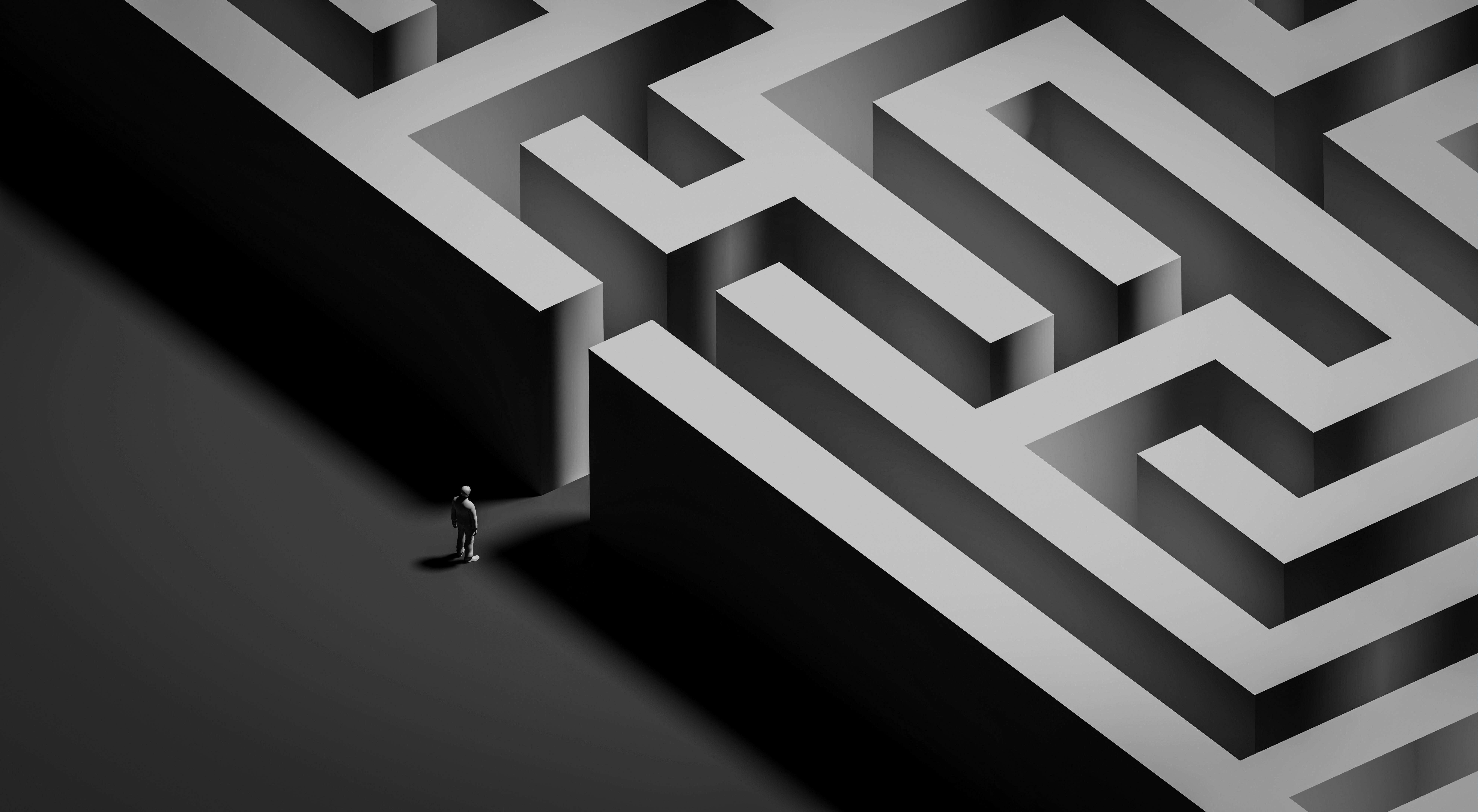 Small figure standing at the entrance of a large black-and-white maze, viewed from above, symbolizing a complex decision path.